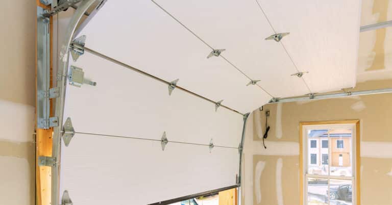 Interior view of a partially open, insulated garage door, highlighting its metal tracks and hardware, in an unfinished garage space."