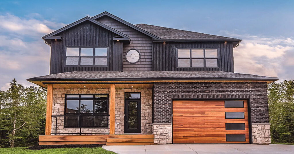 The faux-wood steel garage door by C.H.I. in this image features a striking design that combines natural wood tones with contemporary accents. It consists of horizontal faux-wood panels, which provide warmth and texture, complemented by four rectangular, horizontally aligned windows on the right-hand side. These windows have a modern black frame that contrasts sharply with the wood tones, enhancing the overall aesthetic. The door's clean lines and high-quality craftsmanship align perfectly with the home’s modern farmhouse design, creating a seamless integration with the dark exterior siding and stonework.