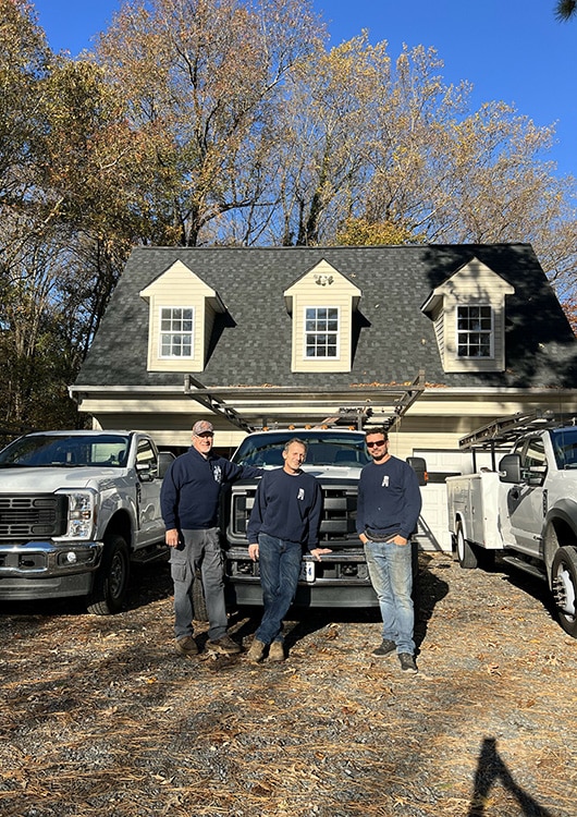 Picture of three Affordable Garage Door technicians dressed in their dark blue company sweatshirts standing in front of gleaming white company trucks.