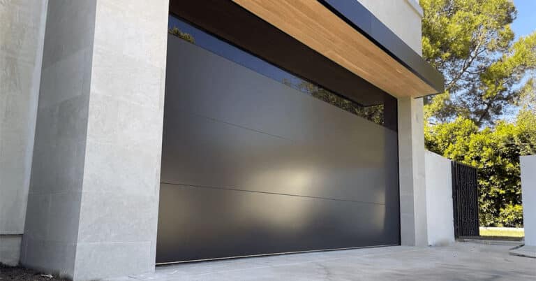 Modern residential garage with a closed, smooth black sectional door from the C.H.I. Sterling model, set within a light stone frame under a wooden overhang.
