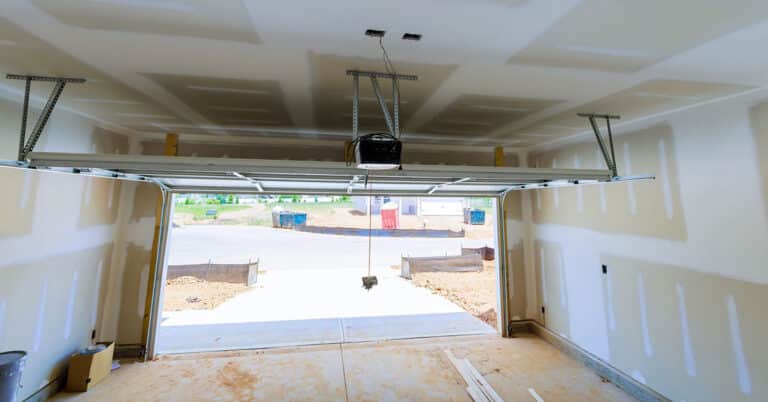Newly built garage with open sectional door, exposed drywall seams and opener.