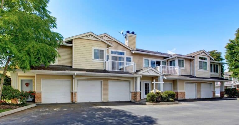 Two-story beige townhomes with six white garage doors, balconies, and a central driveway.